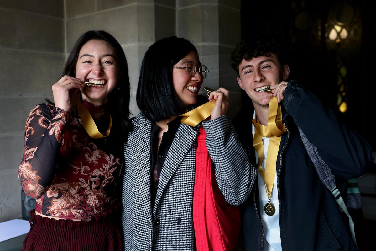 L-R: Estefanía Izarnótegui ’26, Pang Pongsirirushakun ’25, and Alex Reynolds-Scheel ’25 bite their honors medallions as a joke to see if they're real gold. Photo by Jamie Cotten