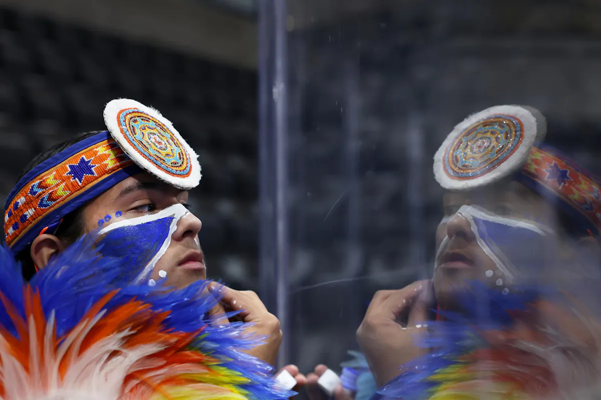 Kobe Moore, 16, who is Pawnee out of Oklahoma, uses the arena's plexiglass to apply face paint before his performance at the NASU Powwow. Photo by Jamie Cotten / Colorado College