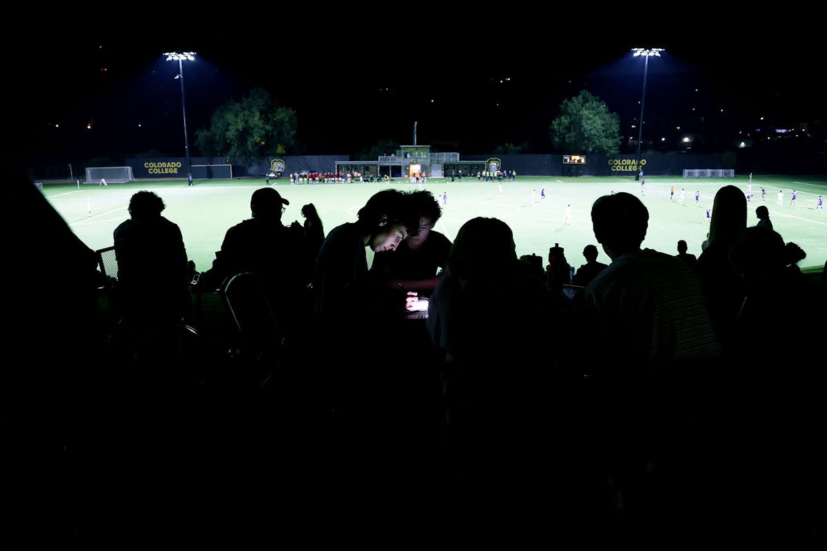 Ben Wolpia '29, center, multitasks between homework and watching a Cutthroats rugby game at Stewart Field during Family Weekend. Photo by Jamie Cotten / Colorado College